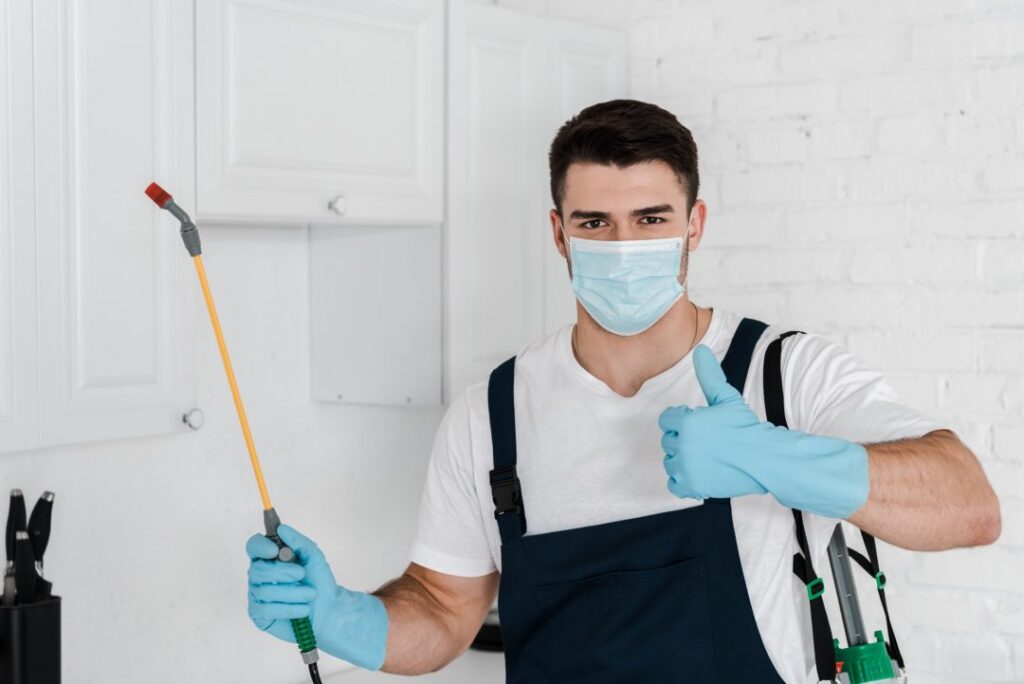exterminator in uniform holding toxic spray and showing thumb up 3